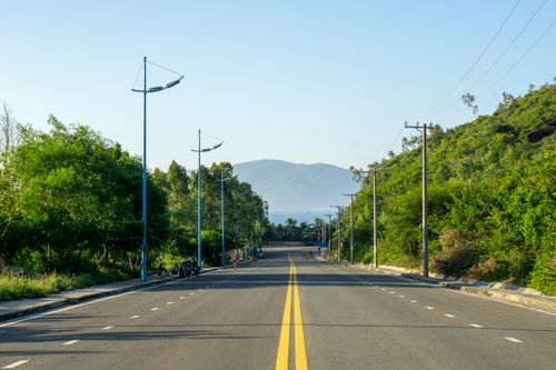 Free Scenic rural road with trees and mountains in the distance under clear blue skies. Stock Photo