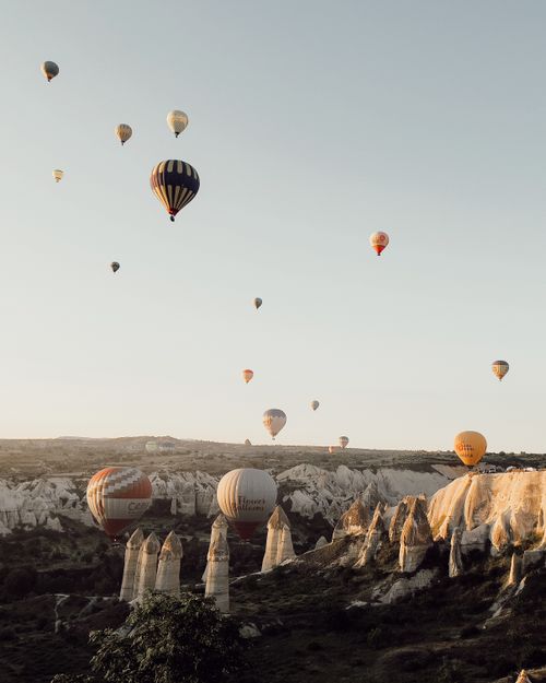 Free Scenic view of hot air balloons floating above Cappadocia's unique rock formations at sunset. Stock Photo