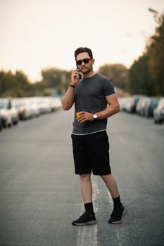 Fashionable man wearing sunglasses and casual outfit, walking and talking on the phone in a city street.