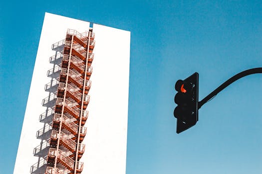 现代城市建筑立面下，蔚蓝的天空映衬着消防通道和红绿灯