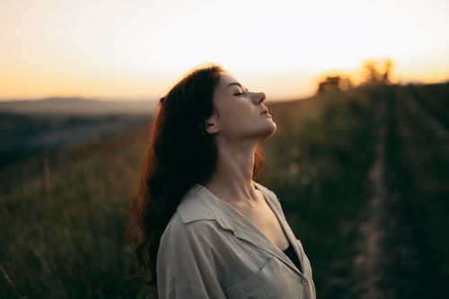 Free Woman standing with eyes closed in a field during sunset, exuding tranquility and peace. Stock Photo