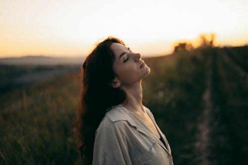 Beautiful Young Woman Standing in the Meadow with Eyes Closed 