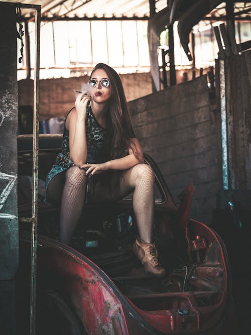 Photo of Woman Sitting on an Abandoned Car Smoking a Cigarette 