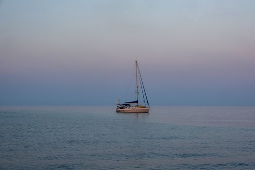 A tranquil sailboat floats on a calm ocean at dawn, enveloped by soft pastel hues.