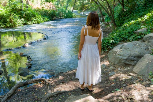Woman in White Dress Standing by River in Forest
