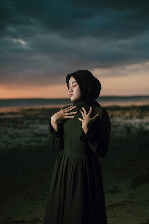 Woman in Black Dress and Hijab on Sea Shore