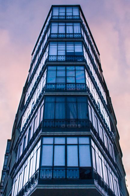 A low-angle view of a modern glass facade high-rise building against a vibrant sky.