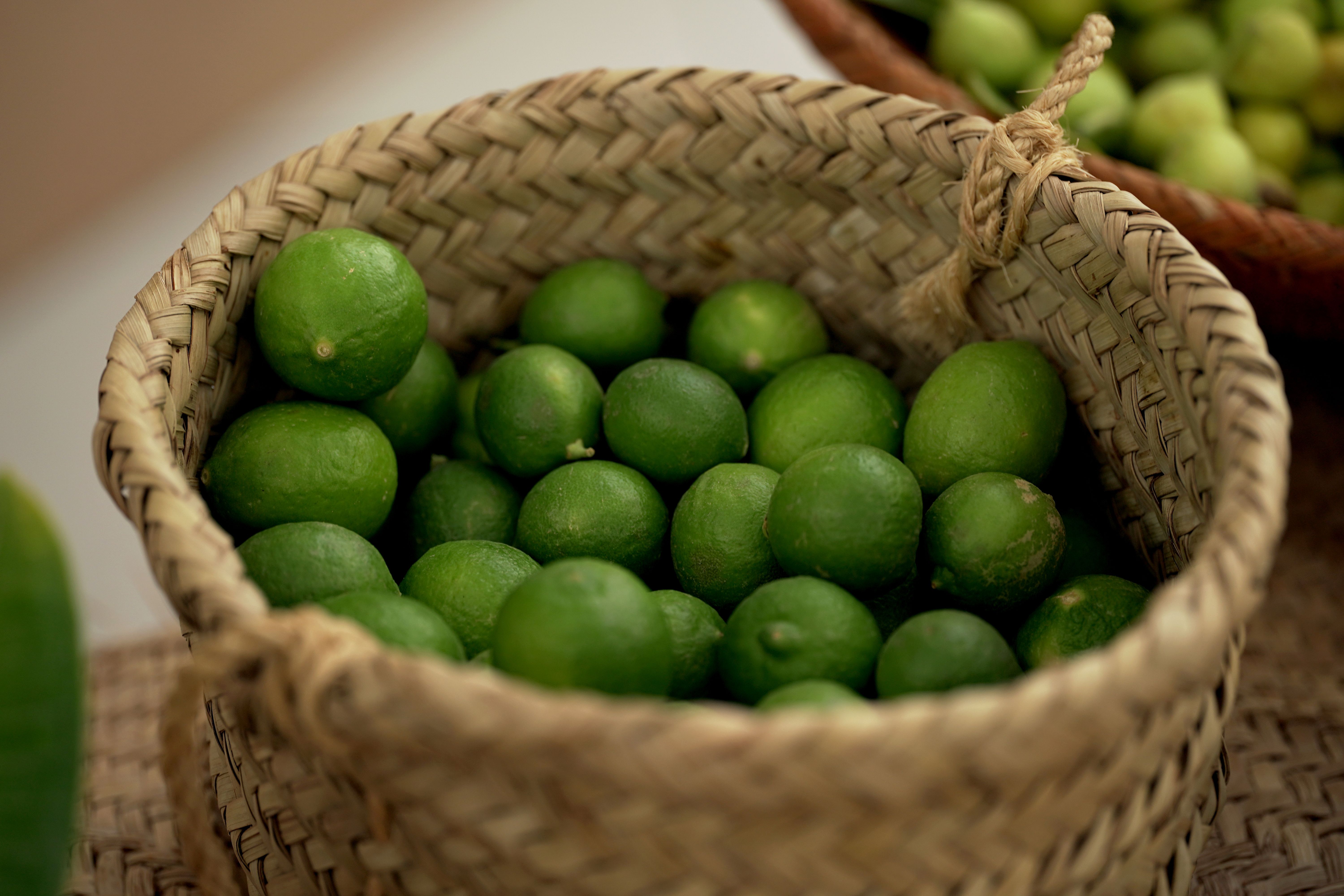 A close-up of fresh green limes in a traditional woven basket, showcasing abundance.