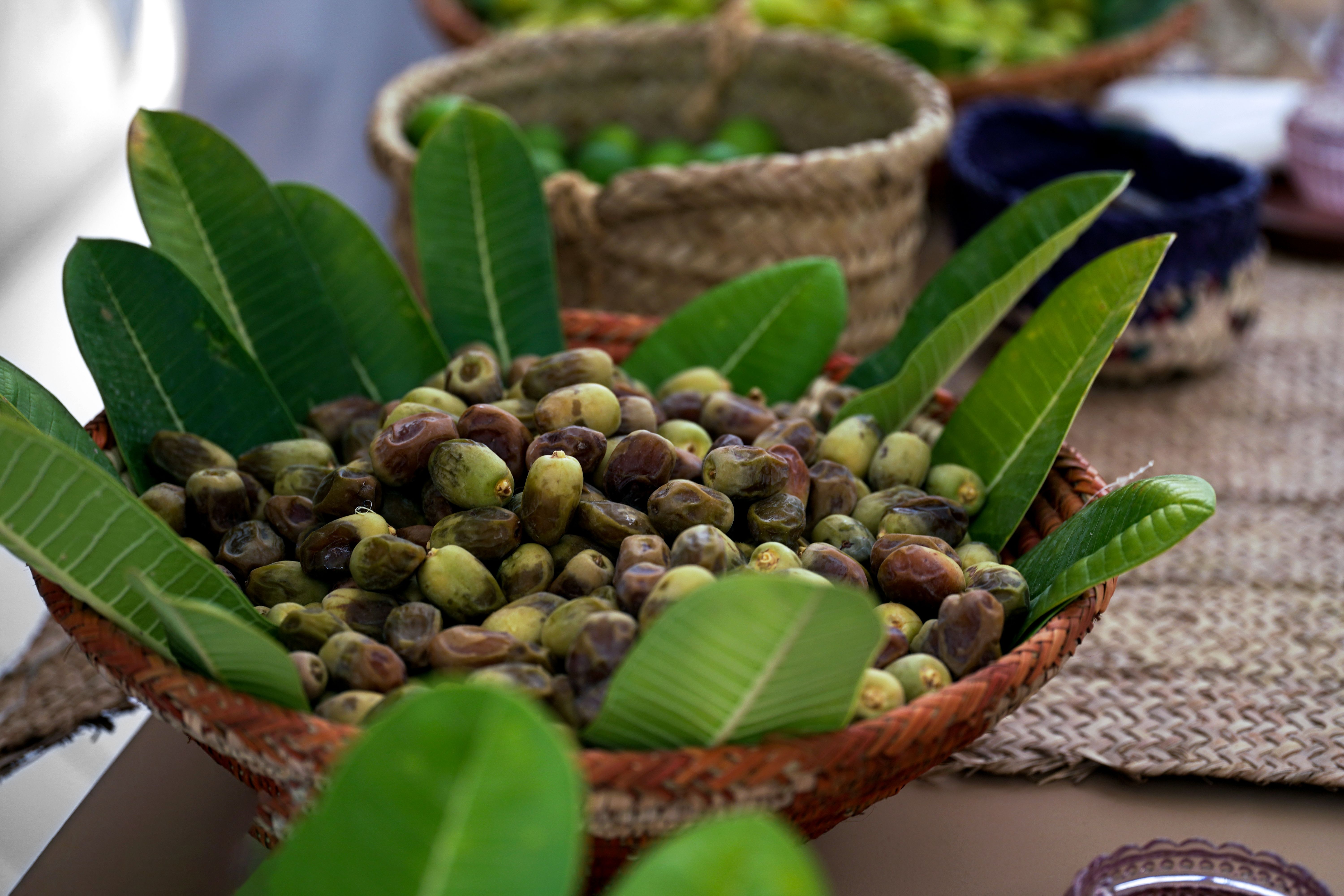 Close-up of fresh dates in a woven basket with green leaves, showcasing rustic charm.