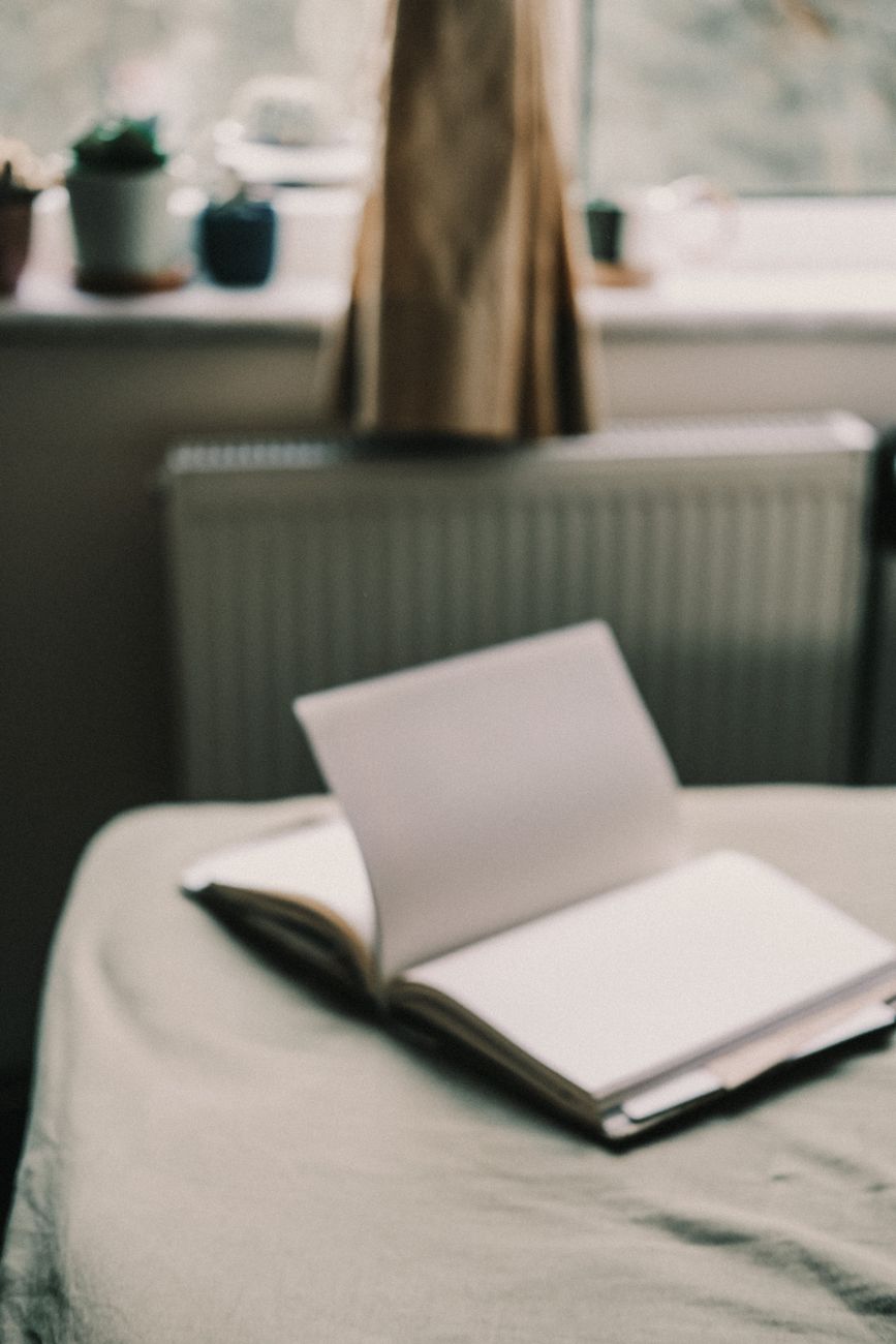 An open notebook beside houseplants suggests the private, hopeful rituals through which people often try to make sense of themselves.