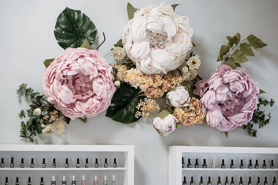 A beautiful arrangement of large artificial flowers adorning a wall above neat shelves with nail polish bottles. A beautiful arrangement of large artificial flowers adorning a wall above neat shelves with nail polish bottles.