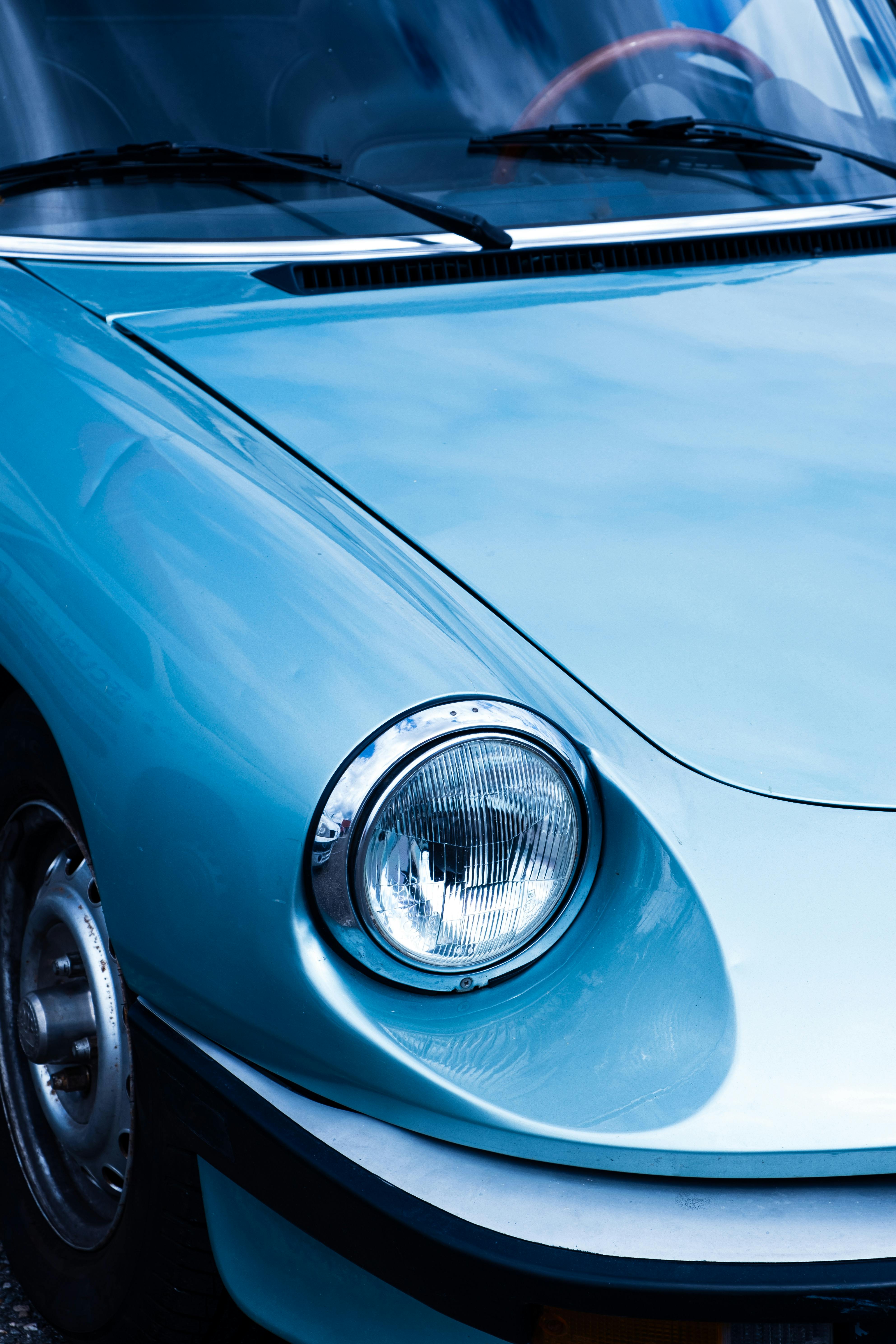A detailed close-up shot of a vintage car's headlight and hood showing sleek, classic design in blue tones.