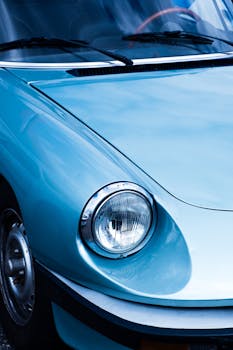 A detailed close-up shot of a vintage car's headlight and hood showing sleek, classic design in blue tones.
