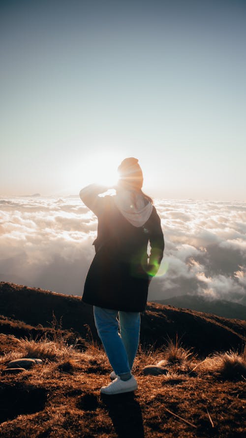 Sunlight over Person Standing on Hilltop over Clouds