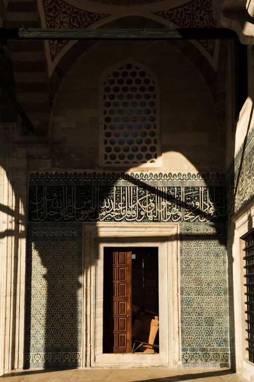 Free A beautifully sunlit mosque entrance displaying intricate Islamic tilework and ornate calligraphy. Stock Photo
