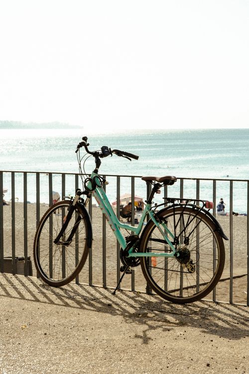 Free A bicycle rests against a railing by the sunlit seaside, offering serene beach and ocean views. Stock Photo