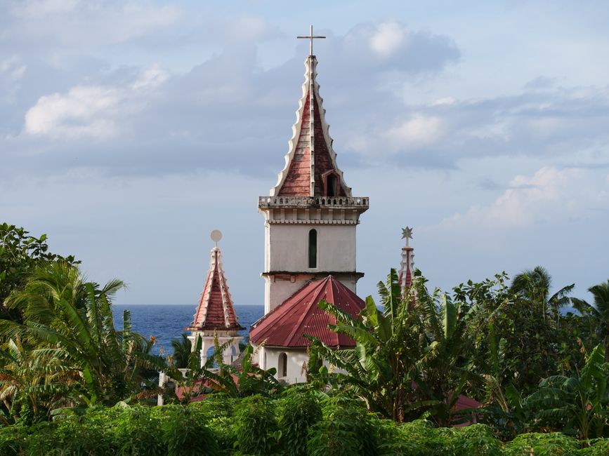 Scenic view of historical church towers surrounded by lush tropical vegetation facing the sea.