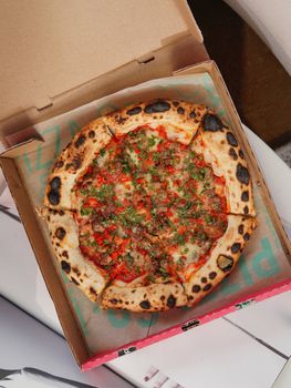 A mouth-watering wood-fired pizza with toppings in an open cardboard box, viewed from above.