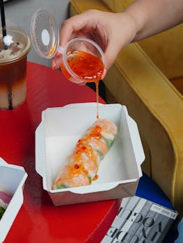 Close-up of a fresh spring roll in a paper box with sauce being poured. Perfect for food enthusiasts.