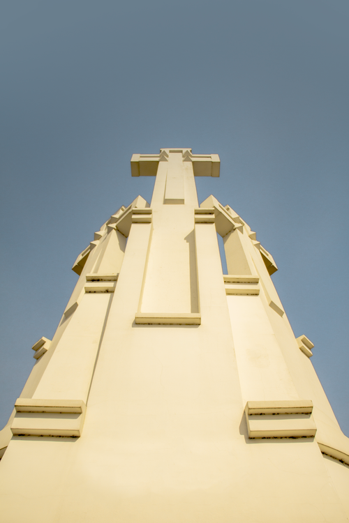 Free A low angle shot of a sunlit cross-shaped statue against a clear sky, emphasizing its architectural design. Stock Photo