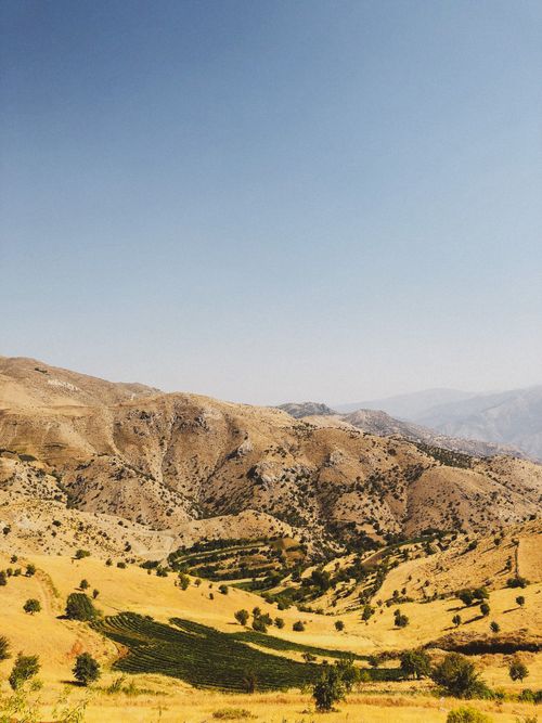 Free Expansive view of arid mountains and valley with patches of green vegetation under clear blue sky. Stock Photo