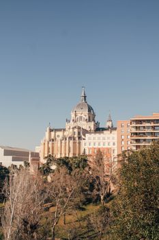 Almudena Cathedral in Madrid, Spain, captured in a sunlit urban setting against a clear sky.