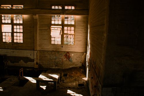 Free Sunlight beams through broken windows in an abandoned factory interior, casting dramatic shadows. Stock Photo