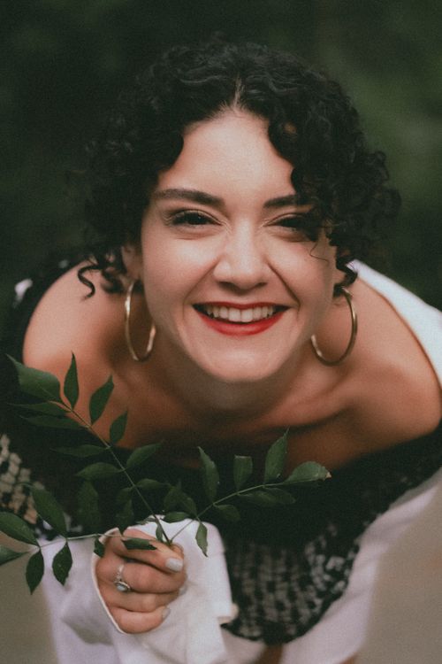 Free Portrait of a smiling woman holding green leaves in an outdoor setting. Stock Photo