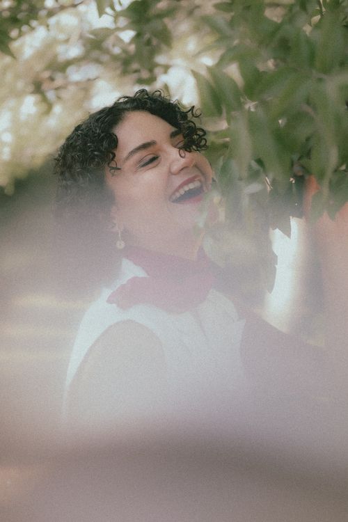 Free A cheerful woman with curly hair and neck scarf enjoys a serene moment in a rural setting. Stock Photo