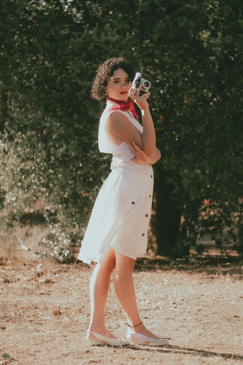 Free Stylish woman holding a vintage camera in a sunny outdoor setting. Stock Photo