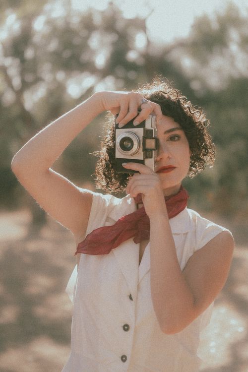 Free Artistic portrait of a woman holding a retro camera outdoors, exuding a vintage vibe with soft lighting. Stock Photo
