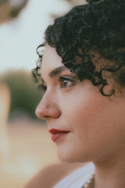 Elegant close-up profile portrait of a woman with curly hair and vivid red lipstick.