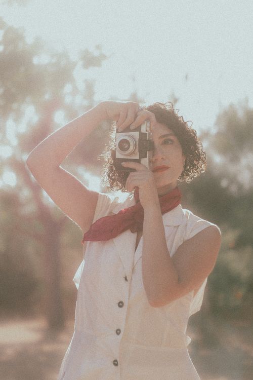 Free A woman in vintage attire takes a photograph outdoors in soft sunlight. Stock Photo