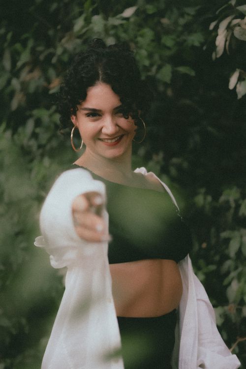Free Young woman in a crop top confidently pointing with a smile outdoors. Stock Photo
