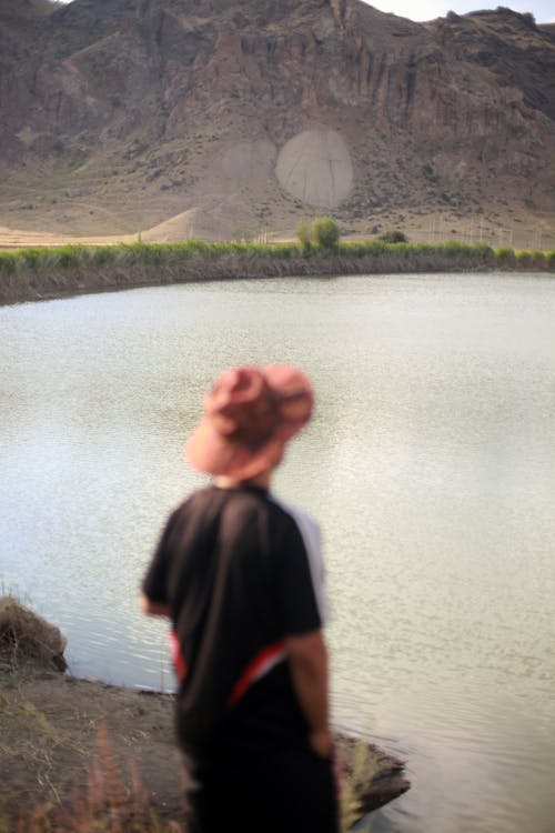 Blurred Photo of a Man Standing and Looking at the View of Mountains and Lake 