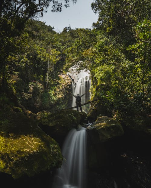 Free Backpacker Standing with Outstretched Arms and Looking at Waterfall  Stock Photo