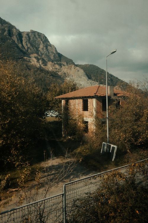 Free Rustic abandoned house surrounded by autumn foliage with a mountain backdrop. Stock Photo