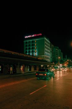 Urban nighttime scene featuring a hotel with neon lights and moving traffic.