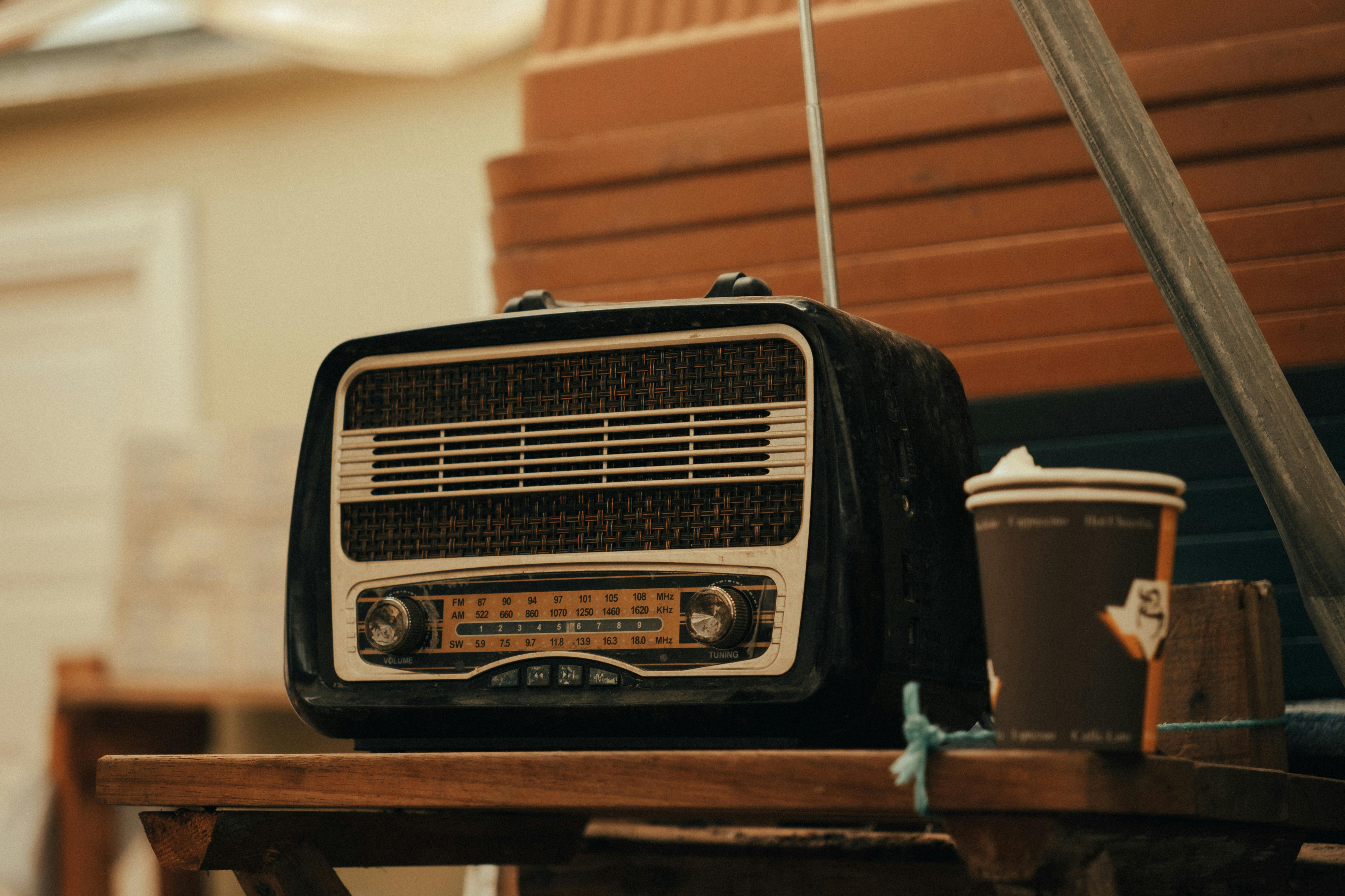 A classic vintage radio placed on a wooden table beside a disposable coffee cup.