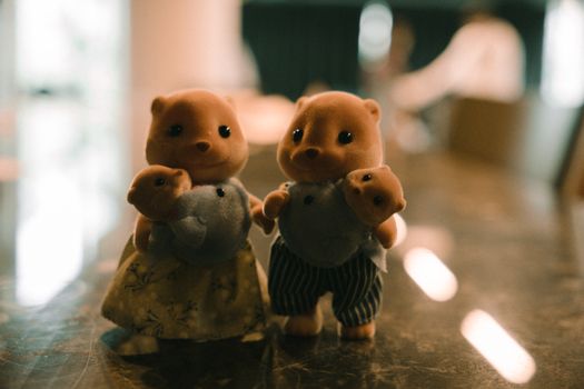 Fuzzy toy animals with baby figures, standing indoors with soft lighting.