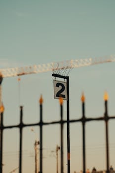 Close-up of a number 2 signpost with urban construction backdrop and fenced decor.