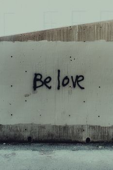 Graffiti reading 'Be Love' on a concrete wall, conveying a message of positivity in an urban environment.