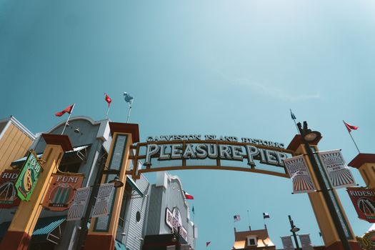 View of the iconic Galveston Island Historic Pleasure Pier entrance under a bright blue sky.