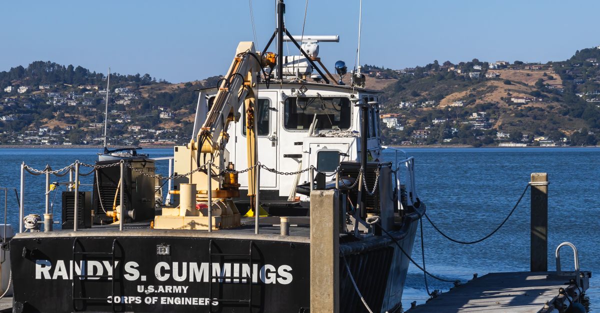 US Army Corps of Engineers vessel docked at pier with scenic hillside view.