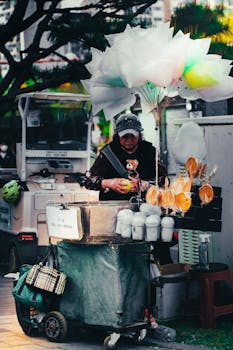 Street vendor selling cotton candy and sweets from a cart in an urban setting.