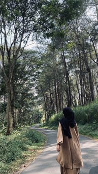 A woman in a hijab walks down a picturesque forest path in Malang, Indonesia.