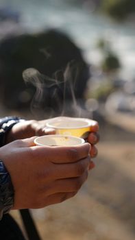 Close-up of hands holding steaming cups of hot drink in an outdoor setting.. close, hands, holding