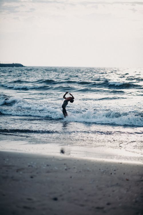 Free Silhouette of a person dancing in ocean waves, backlit by sunrise light. Stock Photo
