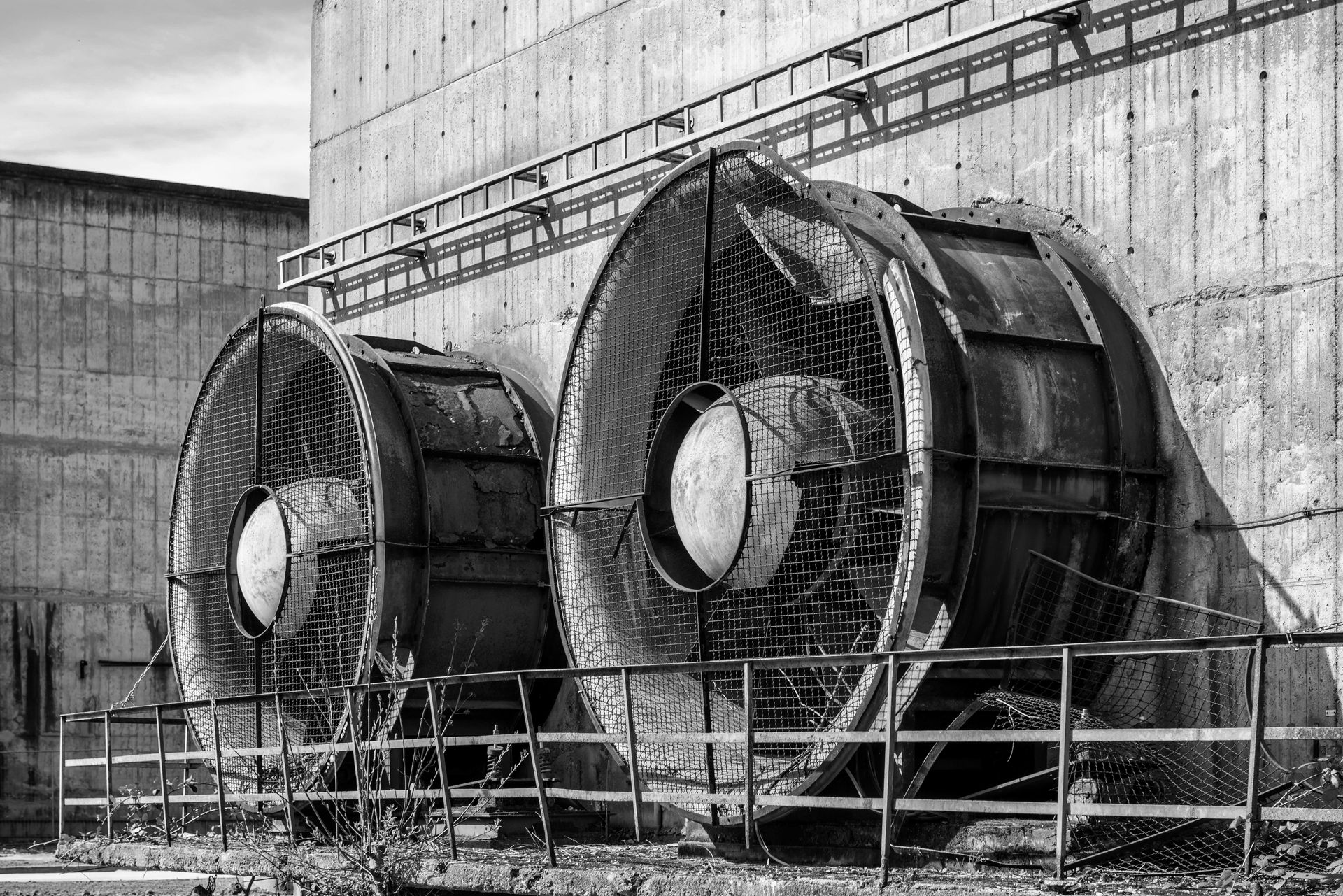 Black and white photo of industrial fans mounted on a concrete wall in an urban environment.