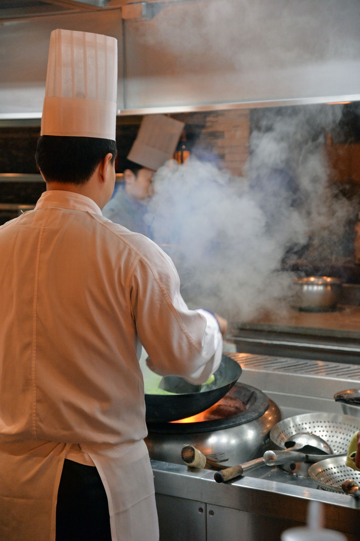 Chefs cooking with woks in a smoky restaurant kitchen